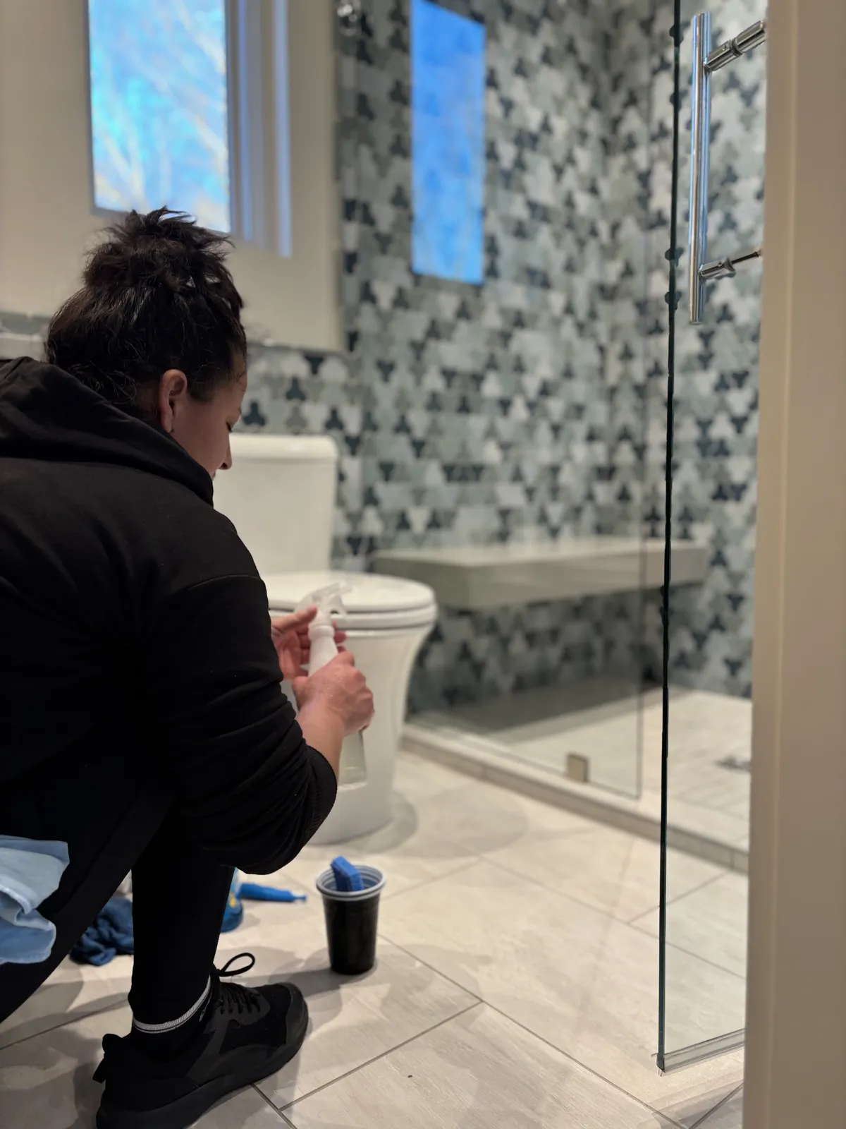Fresh Start crew member cleaning a guest bathroom in a Nashville home, spraying near the toilet by a tiled shower
