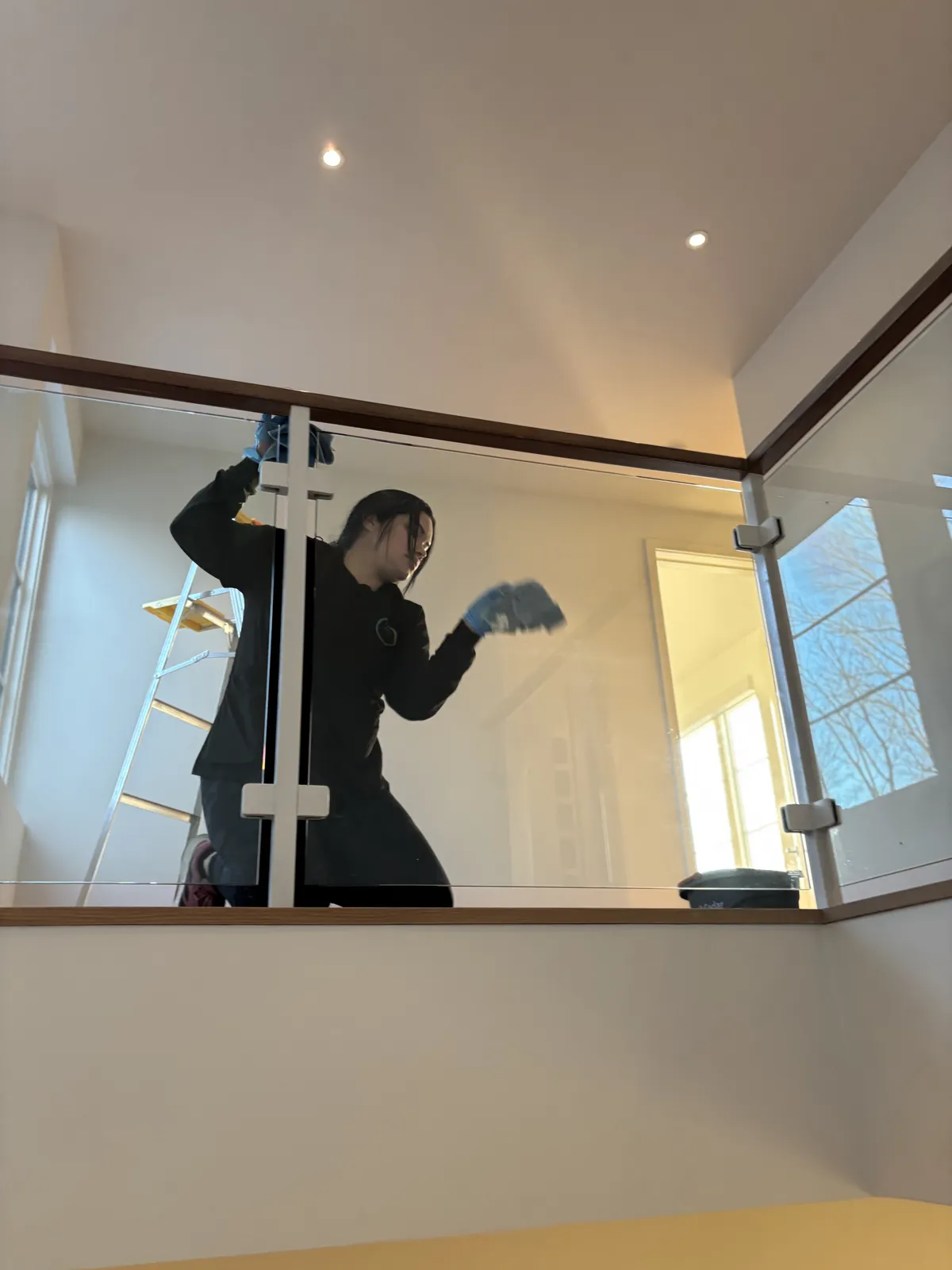 Fresh Start crew member detailing a glass railing panel from a ladder in an empty Nashville home