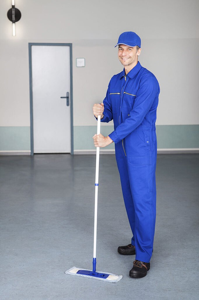 Janitor in blue coveralls mopping industrial floor after demolition