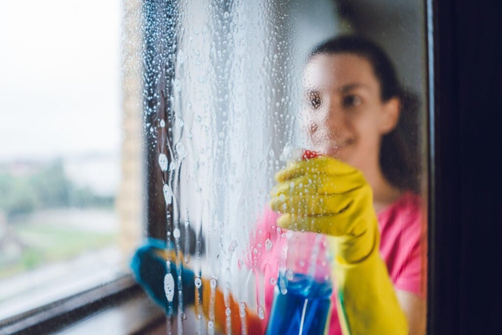 Woman scrubbing window with sponge and spray bottle