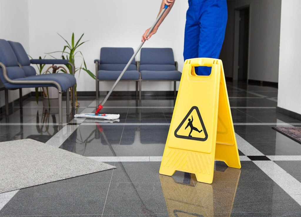 Janitor mopping office lobby floor near wet floor sign