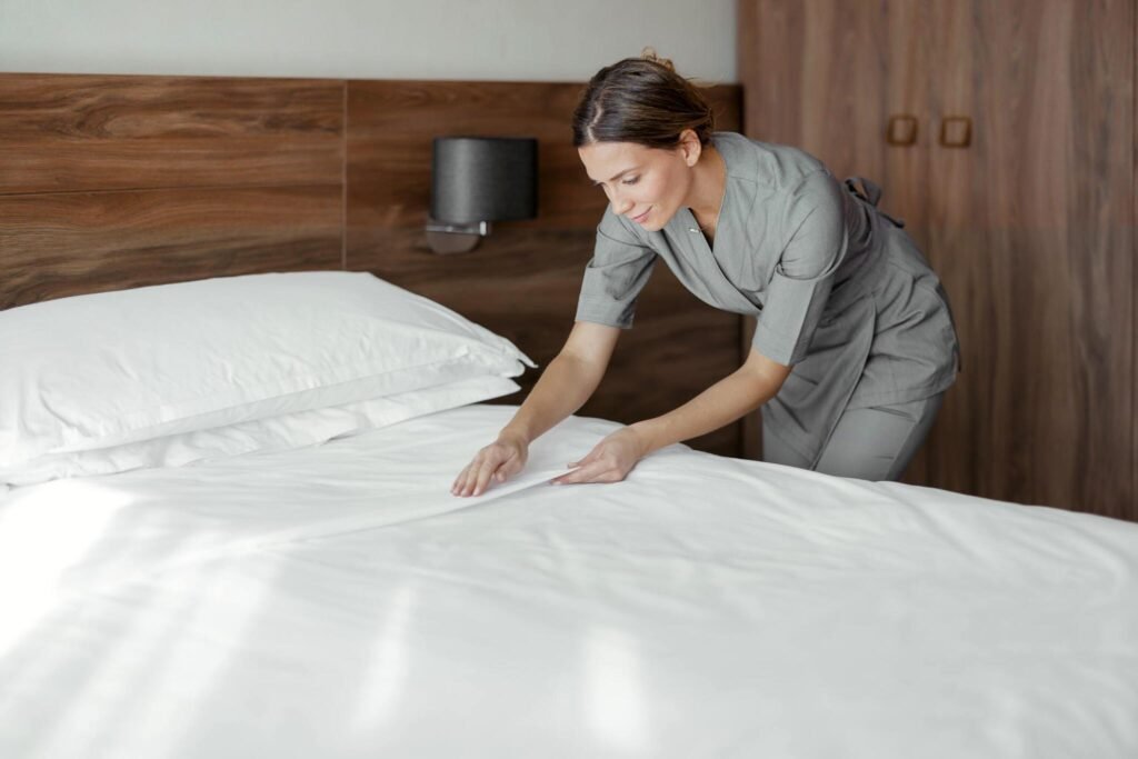 Housekeeper smoothing fresh bed sheets during daily janitorial visit
