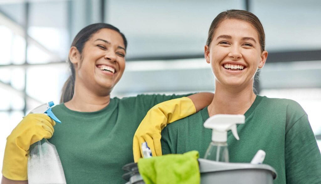 Two smiling cleaners with spray bottles and supplies ready for work