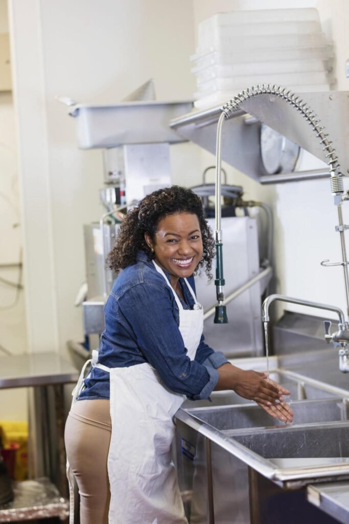 Worker washing hands at commercial kitchen sink after construction cleanup